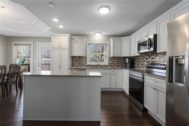 kitchen with appliances with stainless steel finishes, dark wood-style flooring, a kitchen island, and a wealth of natural light