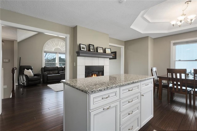 kitchen with dark wood-style flooring, a tiled fireplace, an inviting chandelier, and light stone countertops