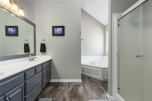 bathroom featuring double vanity, a stall shower, lofted ceiling, wood finished floors, and a bath