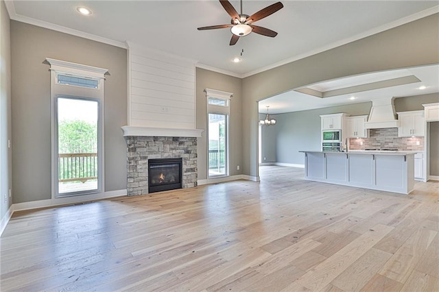 unfurnished living room with crown molding, light wood-type flooring, plenty of natural light, and ceiling fan with notable chandelier