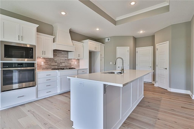 kitchen featuring a kitchen island with sink, stainless steel appliances, a sink, white cabinetry, and light countertops