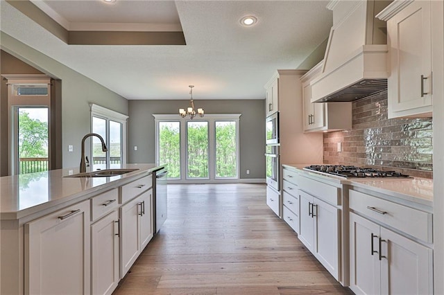 kitchen with premium range hood, a sink, appliances with stainless steel finishes, a center island with sink, and pendant lighting