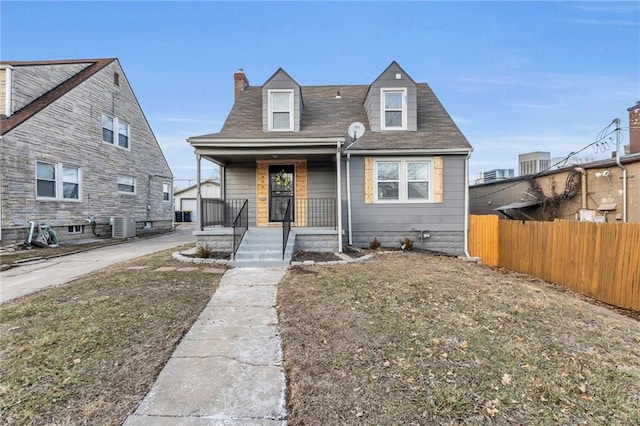 view of front of property featuring cooling unit, covered porch, fence, a chimney, and a front yard