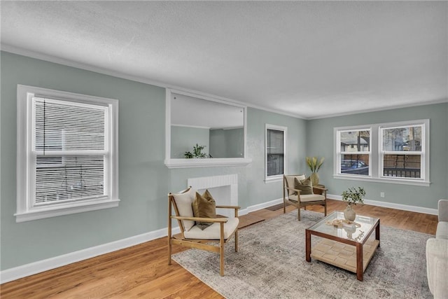 living area with a brick fireplace, crown molding, baseboards, and wood finished floors