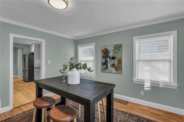 dining room with a healthy amount of sunlight, baseboards, wood finished floors, and ornamental molding