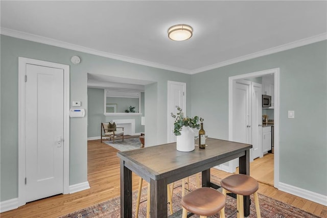 dining room with ornamental molding, light wood-style flooring, and baseboards