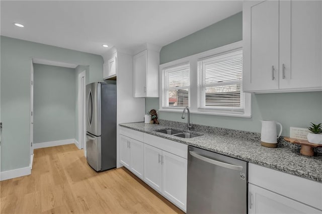 kitchen featuring appliances with stainless steel finishes, light stone counters, light wood-type flooring, white cabinetry, and a sink