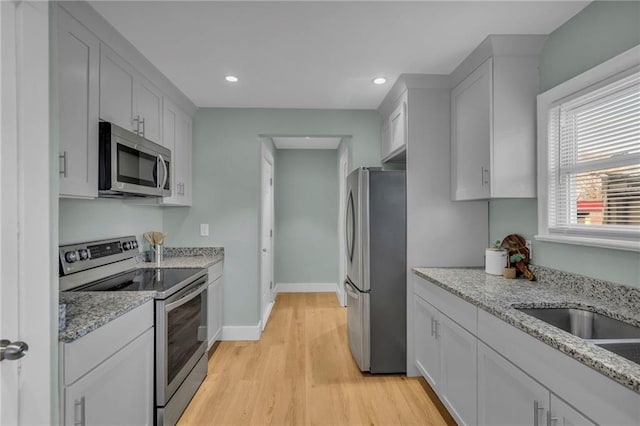 kitchen featuring baseboards, white cabinets, appliances with stainless steel finishes, light stone countertops, and light wood-type flooring