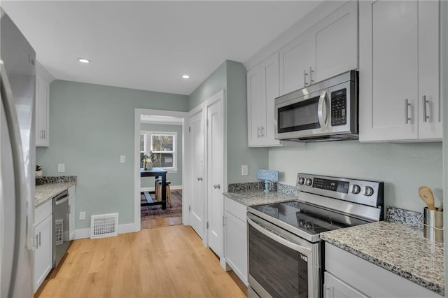 kitchen featuring stainless steel appliances, visible vents, white cabinetry, light stone countertops, and light wood finished floors