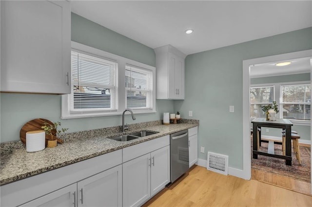 kitchen featuring visible vents, white cabinets, dishwasher, light stone counters, and a sink