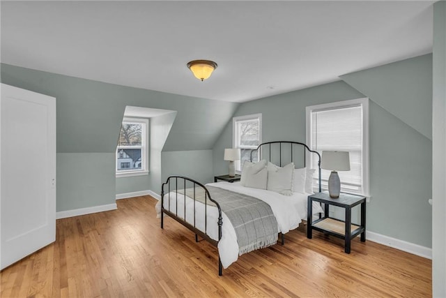 bedroom with light wood-style floors, baseboards, and vaulted ceiling