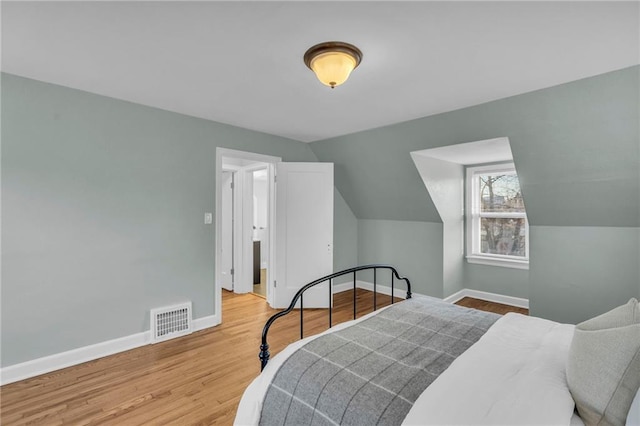 bedroom featuring lofted ceiling, visible vents, baseboards, and wood finished floors