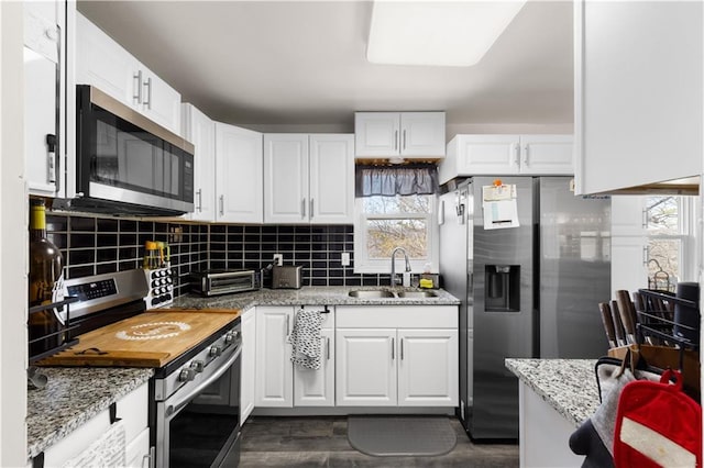 kitchen with light stone countertops, a sink, decorative backsplash, white cabinets, and appliances with stainless steel finishes