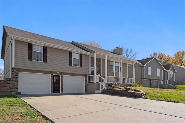 bi-level home featuring a garage, brick siding, driveway, and a chimney