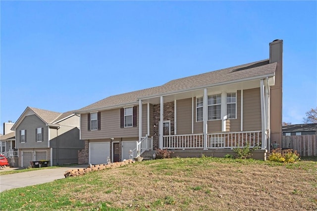 bi-level home featuring a chimney, covered porch, an attached garage, a front yard, and driveway