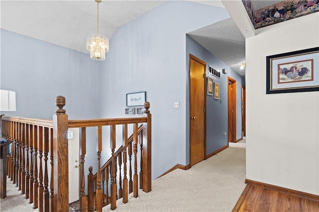 hallway with carpet floors, lofted ceiling, an upstairs landing, a chandelier, and baseboards