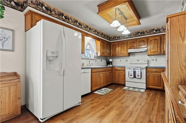 kitchen with white appliances, light wood finished floors, brown cabinets, decorative light fixtures, and under cabinet range hood