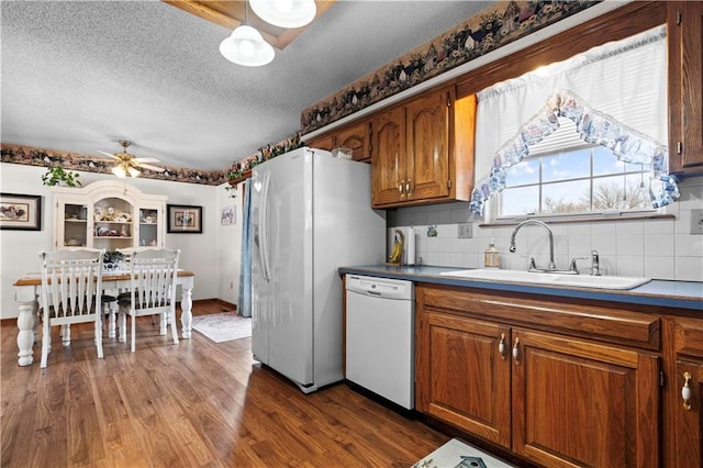 kitchen featuring white appliances, decorative backsplash, brown cabinets, dark wood-type flooring, and a sink