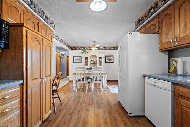 kitchen featuring a ceiling fan, dark countertops, brown cabinets, wood finished floors, and white dishwasher