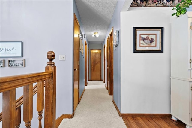 corridor with an upstairs landing, light wood-type flooring, a textured ceiling, and baseboards