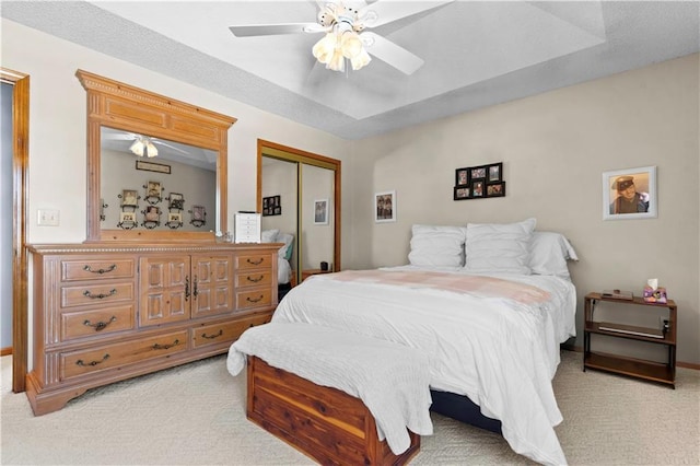 bedroom with a closet, light carpet, ceiling fan, and a raised ceiling