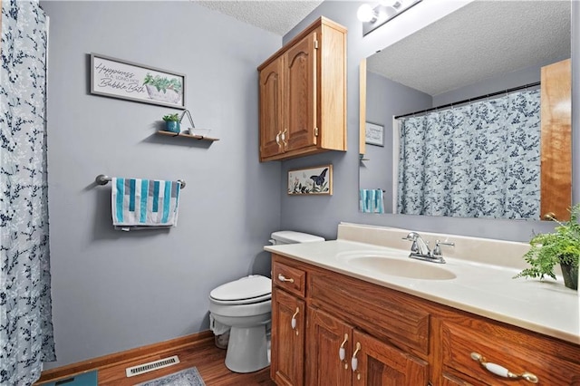 bathroom with a textured ceiling, toilet, wood finished floors, vanity, and baseboards