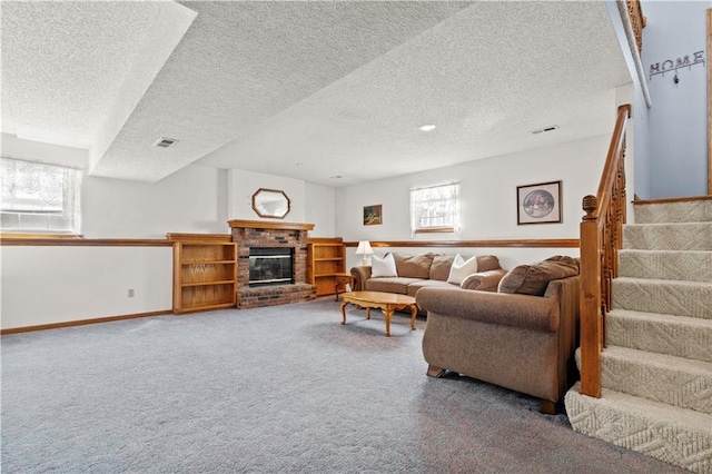 carpeted living room with a textured ceiling, visible vents, baseboards, stairway, and a brick fireplace