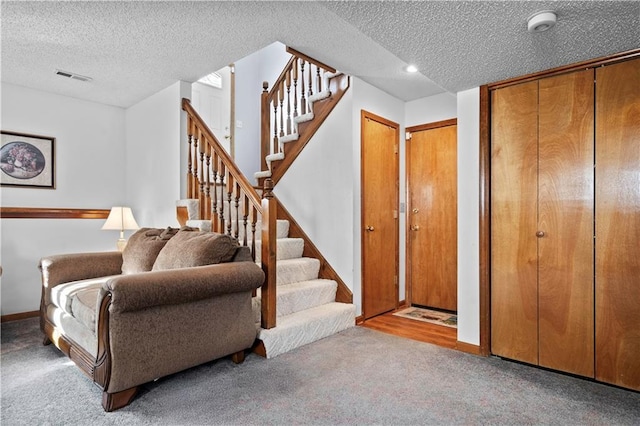 entryway with carpet floors, stairs, visible vents, and a textured ceiling