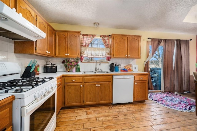 kitchen featuring light wood finished floors, light countertops, a sink, white appliances, and under cabinet range hood