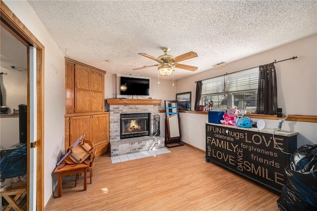 living room featuring a textured ceiling, light wood finished floors, and a brick fireplace