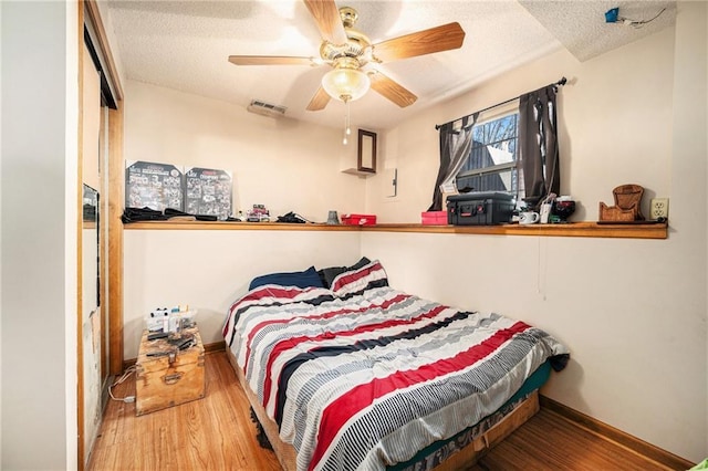 bedroom featuring baseboards, a textured ceiling, visible vents, and wood finished floors