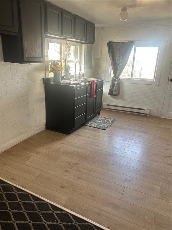 kitchen featuring light wood finished floors, brick wall, a wealth of natural light, and a sink