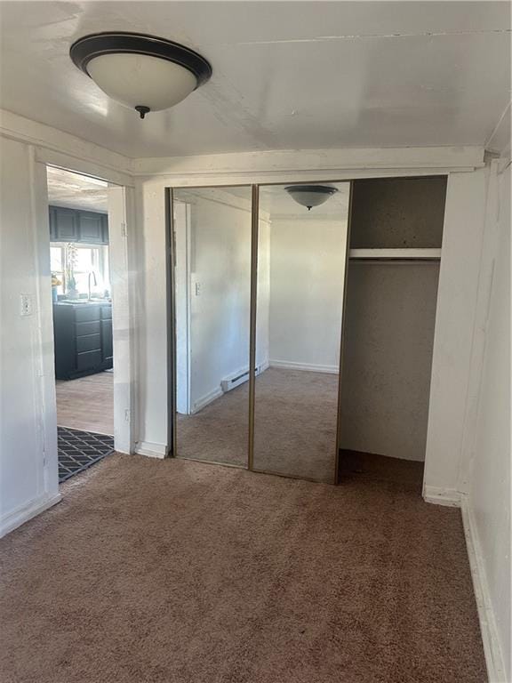 unfurnished bedroom featuring a baseboard heating unit, a closet, baseboards, and carpet flooring