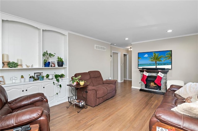 living area featuring a lit fireplace, light wood finished floors, visible vents, and crown molding