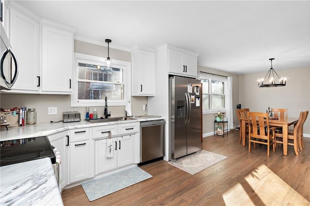 kitchen featuring light stone counters, a sink, white cabinetry, appliances with stainless steel finishes, and decorative light fixtures