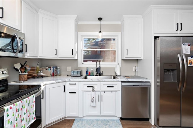 kitchen featuring stainless steel appliances, hanging light fixtures, ornamental molding, white cabinets, and a sink