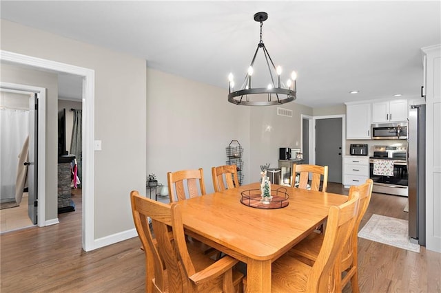 dining room featuring visible vents, a notable chandelier, baseboards, and wood finished floors