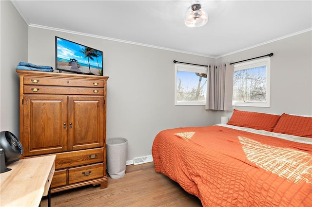 bedroom with baseboards, visible vents, crown molding, and wood finished floors