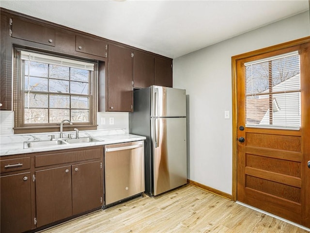 kitchen with a sink, stainless steel appliances, light wood-style floors, light countertops, and dark brown cabinets