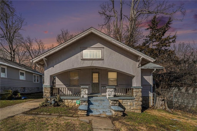 view of front of house with covered porch, fence, and stucco siding