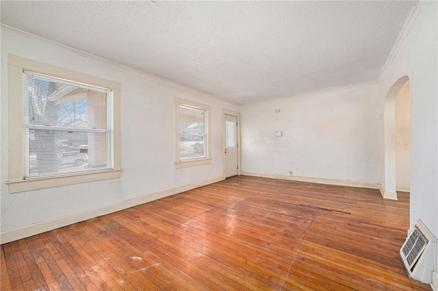 spare room featuring ornamental molding, arched walkways, a textured ceiling, and hardwood / wood-style flooring