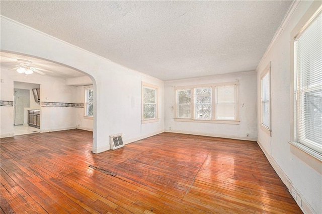 empty room with arched walkways, crown molding, a textured ceiling, and hardwood / wood-style flooring