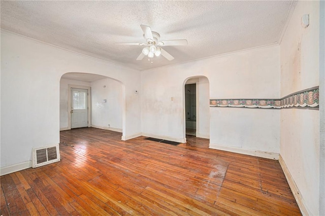 unfurnished room featuring arched walkways, visible vents, ornamental molding, a textured ceiling, and hardwood / wood-style floors