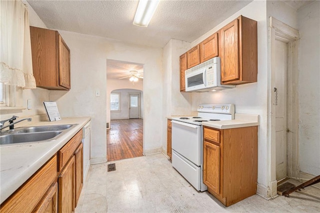 kitchen featuring arched walkways, white appliances, a sink, light countertops, and brown cabinets