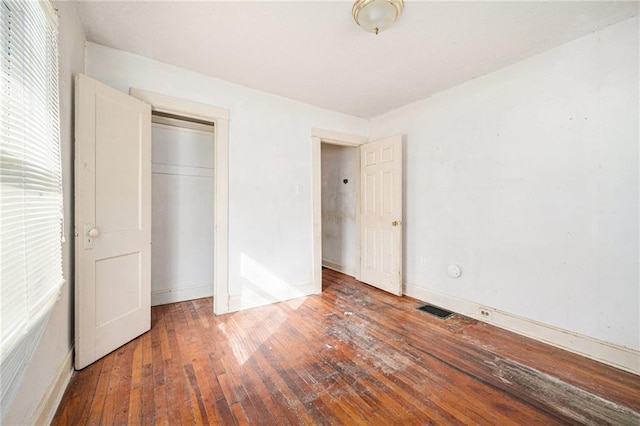 unfurnished bedroom with a closet, wood-type flooring, visible vents, and baseboards