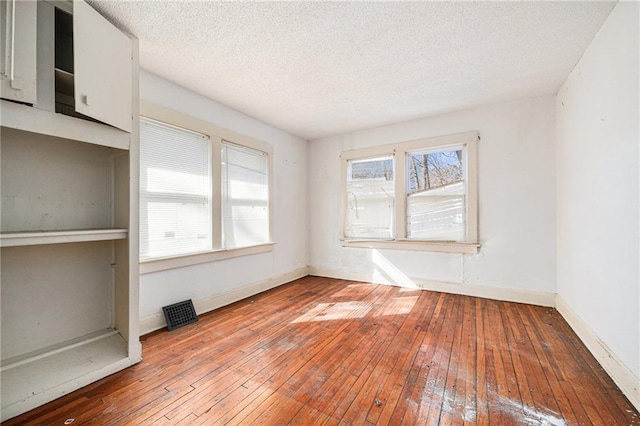 spare room with wood-type flooring, visible vents, baseboards, and a textured ceiling