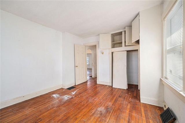 unfurnished bedroom featuring hardwood / wood-style flooring, a closet, visible vents, and baseboards