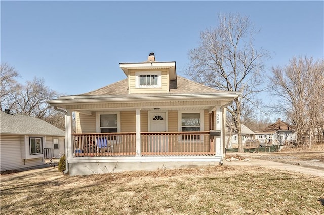 bungalow with covered porch, a shingled roof, a chimney, and a front yard