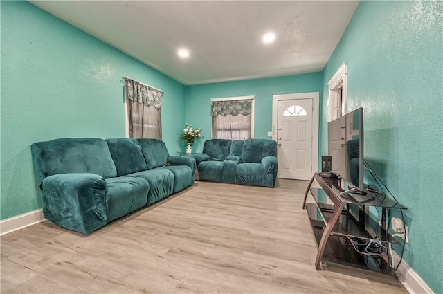 living room featuring light wood-type flooring, a textured wall, and baseboards