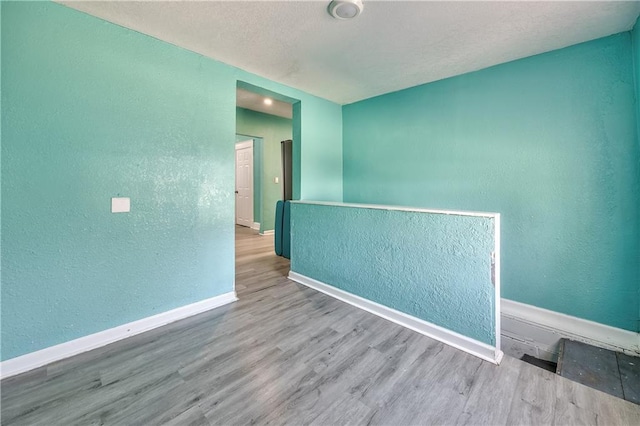 unfurnished room with baseboards, wood finished floors, and a textured wall